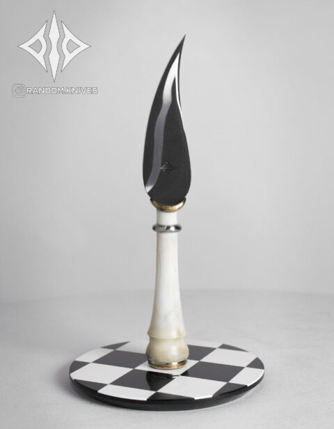 Cuchillo conceptual Alfil con hoja curva negra y cabo blanco sobre base de ajedrez